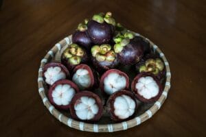 A basket of fresh mangosteen fruit displayed on a wooden table, emphasizing tropical freshness.