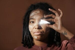 A black woman holds a mirror shard, featuring affirming messages on skin. Studio shot.