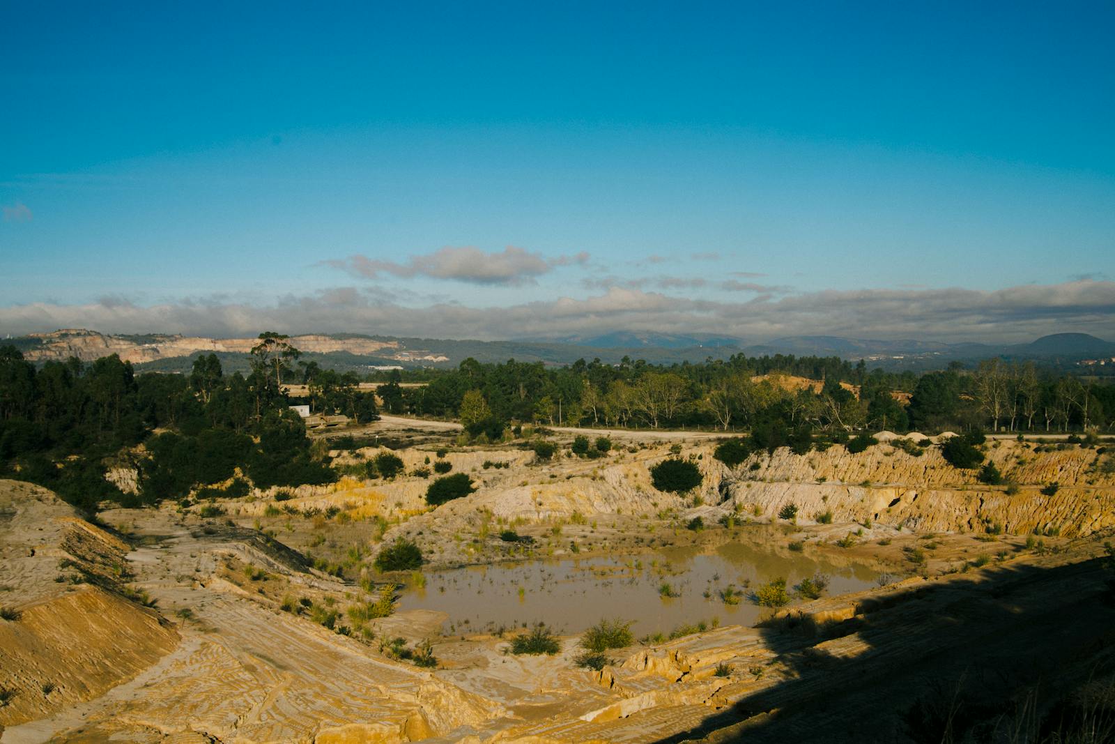 Serene quarry landscape with clear blue skies, surrounded by lush forest and rocky terrain. jas auji laboratorium limbah tambang. mining laboratory waste testing