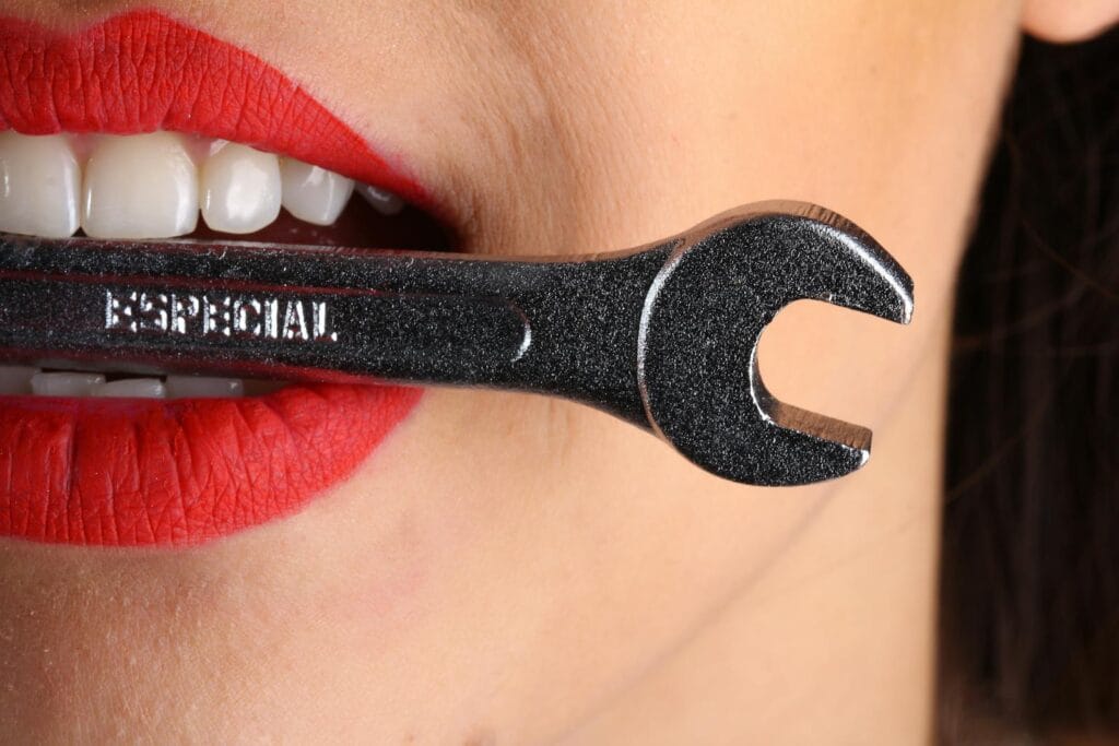 A close-up shot of red lips holding a shiny wrench with bold red lipstick. whitening toothpaste.