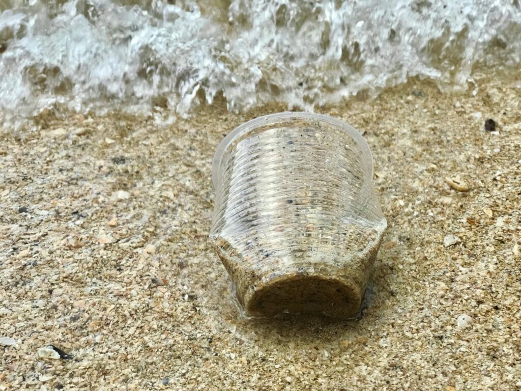 Close-up of a plastic cup on the sandy shore in Malaysia, highlighting pollution issues. mikroba ekstremofil.