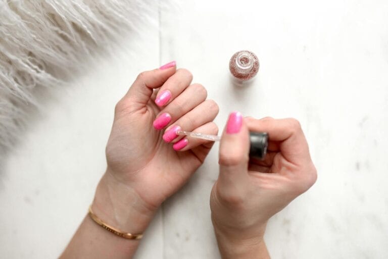 Close-up of a woman applying glitter nail polish to manicured pink fingernails. kutek kuku. nail polish.