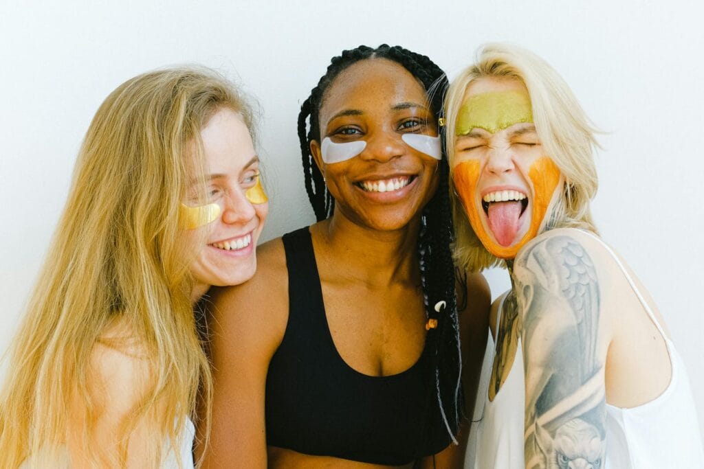 Three diverse women having fun with colorful skincare masks, embodying friendship and joy. skincare natural, skincare organik, skincare sintetik. 