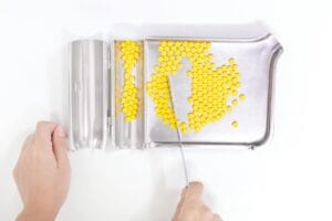 Pharmacy technician organizing yellow pills on a stainless steel tray.