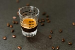 Espresso shot in a measuring glass surrounded by coffee beans, captured in a minimalist style. kafein, cafein.