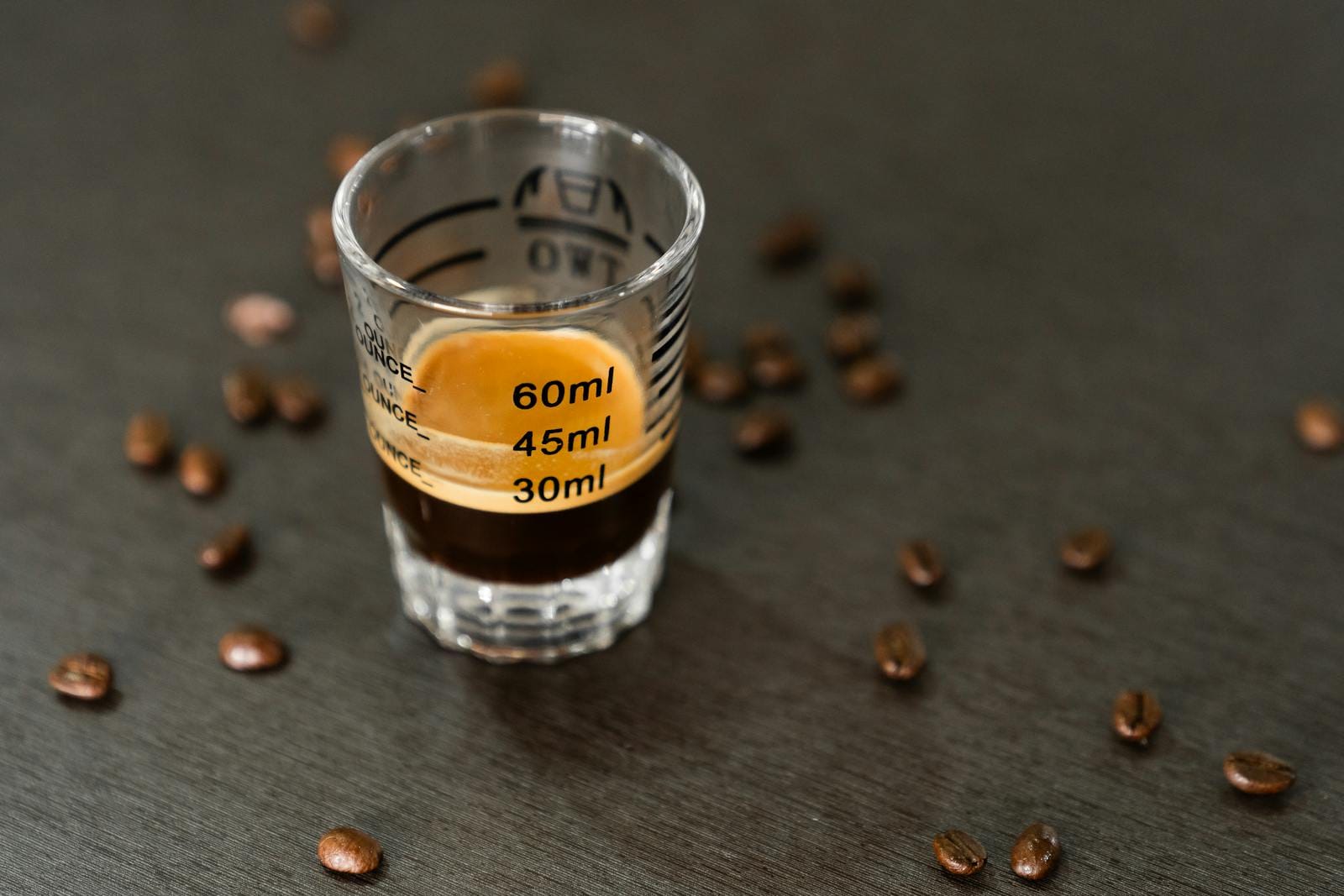Espresso shot in a measuring glass surrounded by coffee beans, captured in a minimalist style. kafein, cafein.