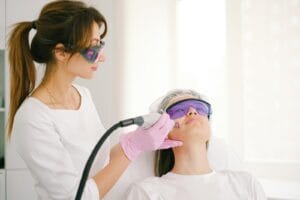 A cosmetologist performing laser treatment on a woman in a clinic setting. krim dokter. Doctor-Prescribed Creams
