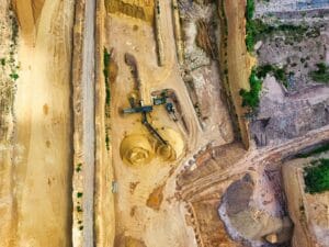 An aerial shot of an open-pit mine with machinery and pathways visible, surrounded by landscape. tailings,