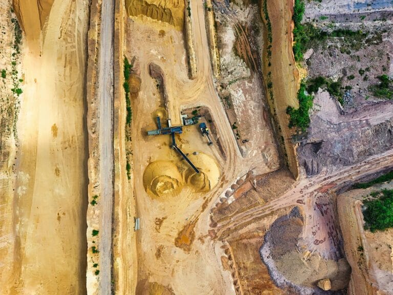 An aerial shot of an open-pit mine with machinery and pathways visible, surrounded by landscape. tailings,