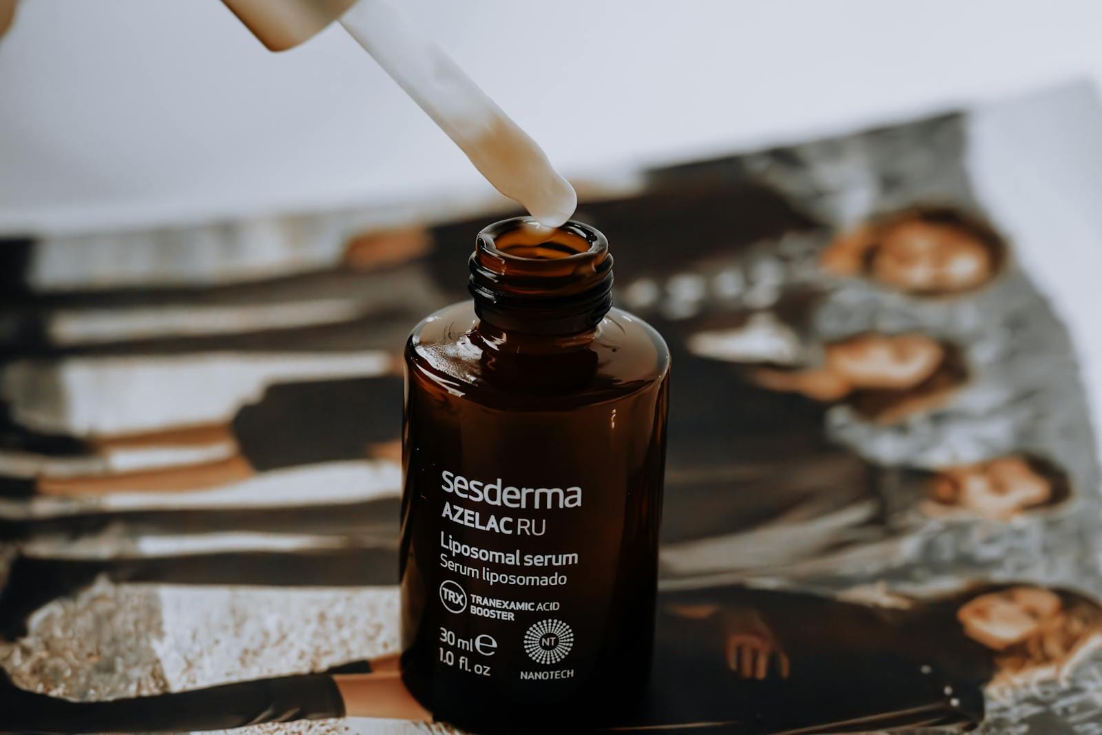 A liposomal serum bottle with a dropper placed on a magazine with blurred background. serum eksfoliasi. Exfoliating Serums