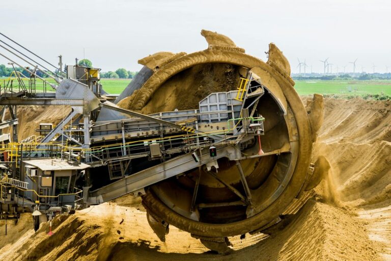 A large bucket wheel excavator working in an open pit mine against a green landscape. Limbah Tambang Emas. gold mine waste