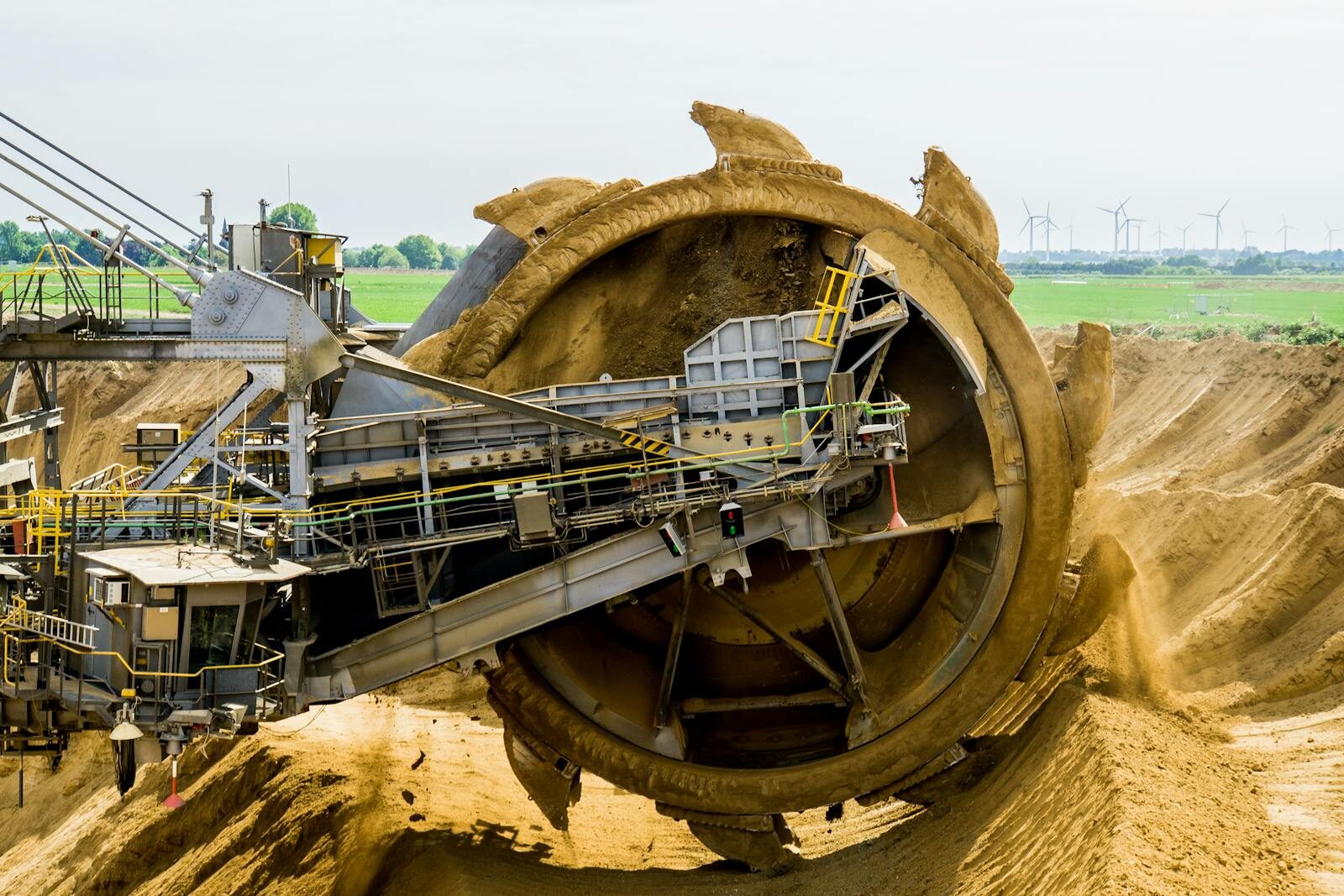 A large bucket wheel excavator working in an open pit mine against a green landscape. Limbah Tambang Emas. gold mine waste
